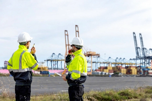 دو فرد که کاپشن گرم کار پوشیده و کلاه ایمنی دارند در پروژه ساختمانی ایستاده اند