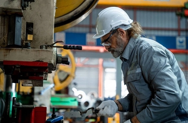 فردی در حال کار کردن با دستگاه صنعتی در حالی که کاپشن کار و لوازم ایمنی به تن دارد